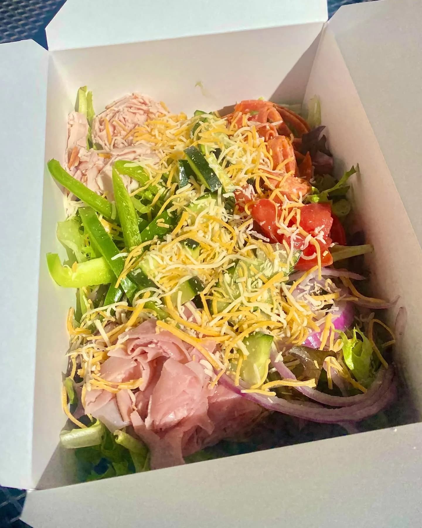 A chef-style salad in a to-go box with ham, turkey and shredded cheese