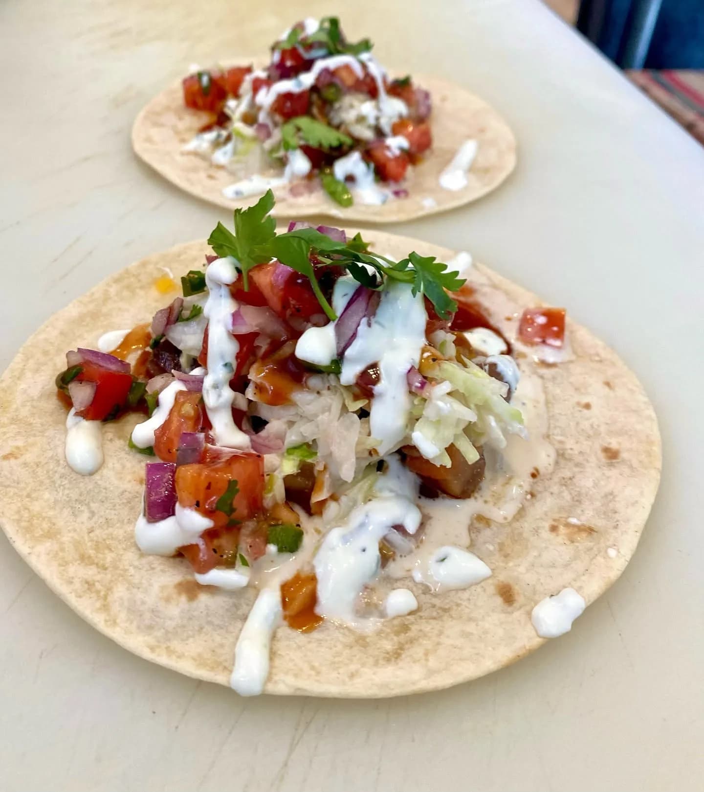 Two tacos topped with pico, slaw and a white drizzle